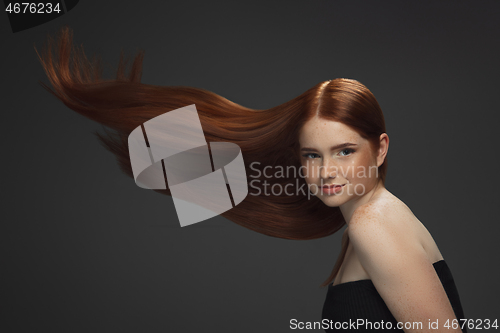 Image of Beautiful model with long smooth, flying red hair isolated on dark studio background.