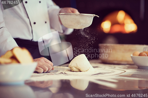 Image of chef sprinkling flour over fresh pizza dough