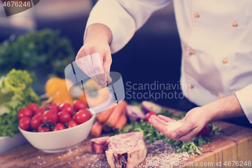 Image of Chef putting salt on juicy slice of raw steak