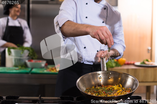 Image of chef putting spices on vegetables in wok