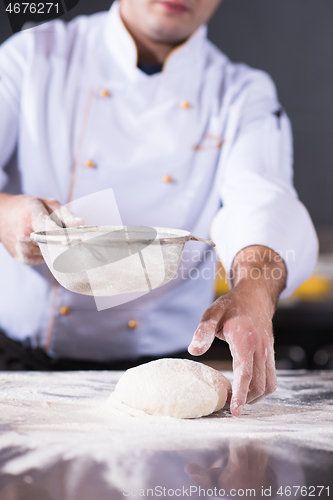 Image of chef sprinkling flour over fresh pizza dough