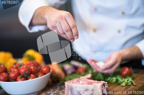 Image of Chef putting salt on juicy slice of raw steak