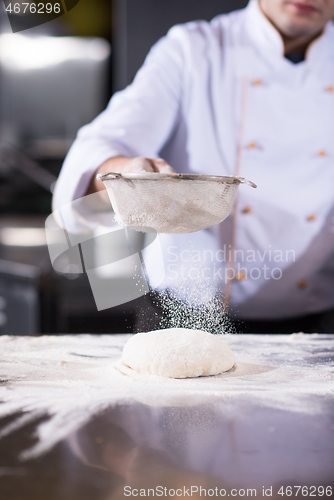 Image of chef sprinkling flour over fresh pizza dough