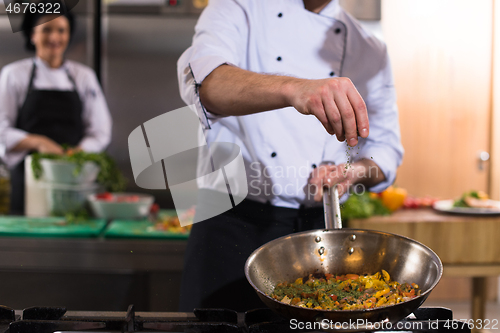 Image of chef putting spices on vegetables in wok