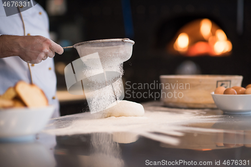 Image of chef sprinkling flour over fresh pizza dough