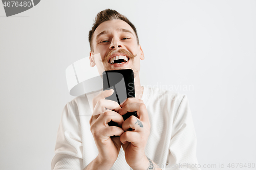 Image of Young handsome man showing smartphone screen isolated on gray background in shock with a surprise face