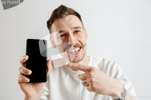 Image of Young handsome man showing smartphone screen isolated on gray background in shock with a surprise face