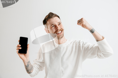 Image of Young handsome man showing smartphone screen isolated on gray background in shock with a surprise face