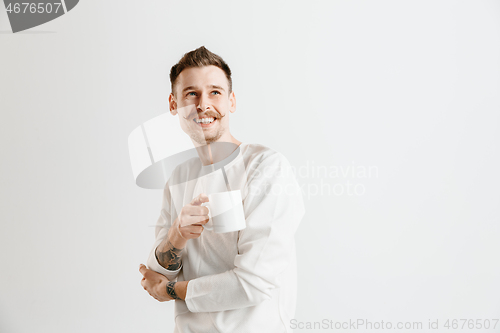 Image of Taking a coffee break. Handsome young man holding coffee cup while standing against gray background