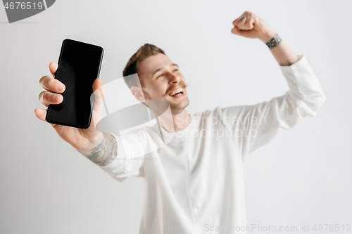 Image of Young handsome man showing smartphone screen isolated on gray background in shock with a surprise face