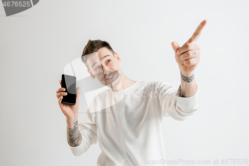 Image of Young handsome man showing smartphone screen isolated on gray background in shock with a surprise face