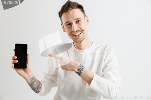 Image of Young handsome man showing smartphone screen isolated on gray background in shock with a surprise face