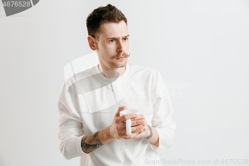 Image of Taking a coffee break. Handsome young man holding coffee cup while standing against gray background
