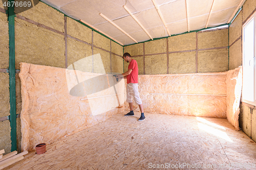 Image of A worker is installing a roll of insulation in the construction of a country house