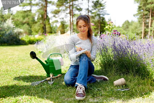 Image of young woman writing to notebook at summer garden