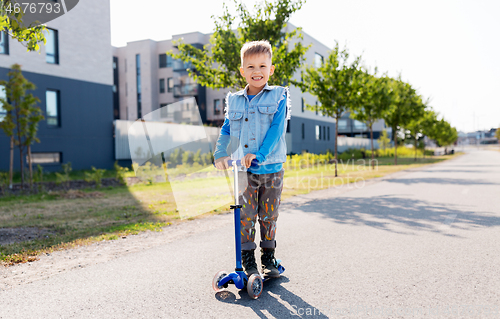 Image of happy little boy riding scooter in city