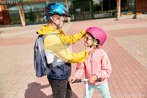 Image of school boy fastening girl\'s helmet for scooter