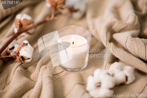 Image of burning candle and cotton flower on blanket