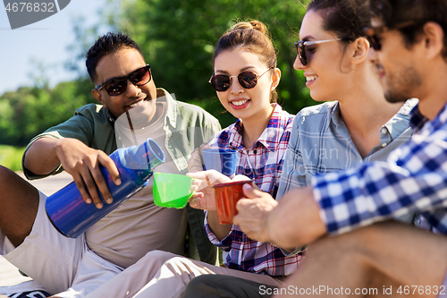 Image of happy friends drinking tea from thermos in summer