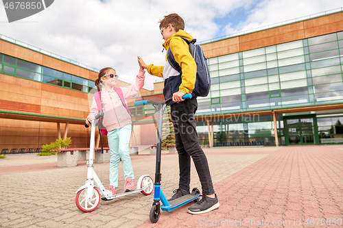 Image of happy school children with backpacks and scooters