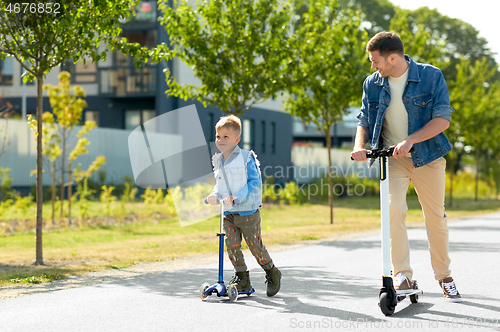 Image of father and little son riding scooters in city