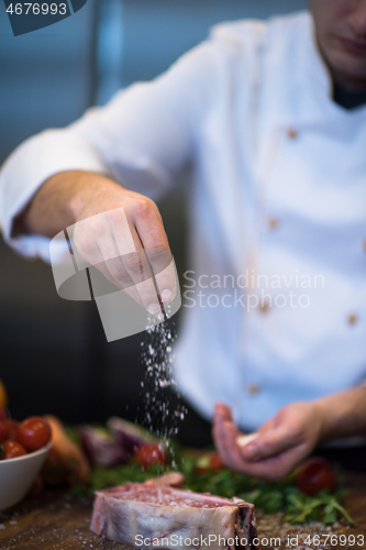 Image of Chef putting salt on juicy slice of raw steak