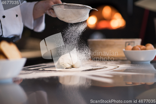 Image of chef sprinkling flour over fresh pizza dough