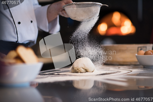 Image of chef sprinkling flour over fresh pizza dough