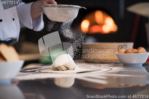 Image of chef sprinkling flour over fresh pizza dough