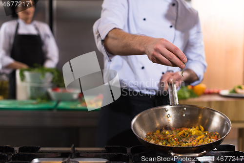 Image of chef putting spices on vegetables in wok