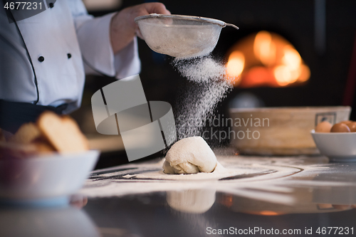 Image of chef sprinkling flour over fresh pizza dough