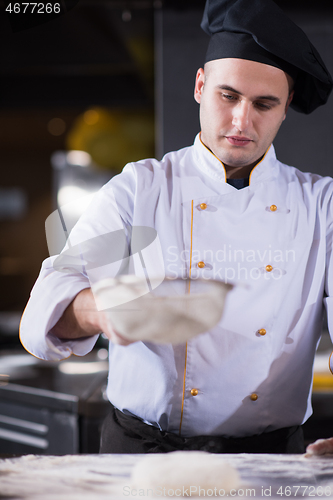 Image of chef sprinkling flour over fresh pizza dough