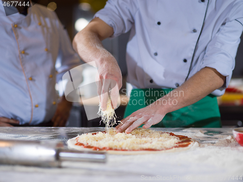 Image of chef sprinkling cheese over fresh pizza dough