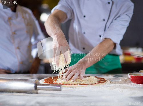 Image of chef sprinkling cheese over fresh pizza dough