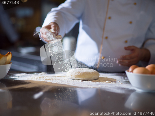 Image of chef sprinkling flour over fresh pizza dough