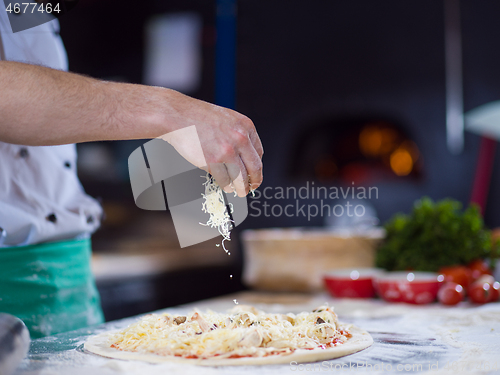 Image of chef sprinkling cheese over fresh pizza dough