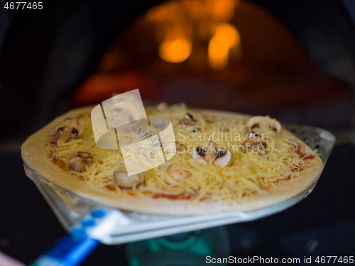 Image of chef putting delicious pizza to brick wood oven