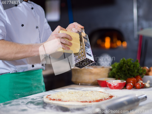 Image of chef sprinkling cheese over fresh pizza dough