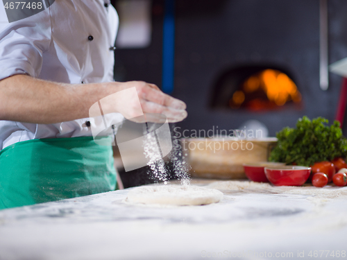 Image of chef sprinkling flour over fresh pizza dough