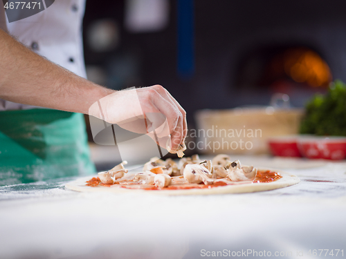 Image of chef putting fresh mushrooms on pizza dough