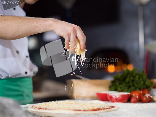 Image of chef sprinkling cheese over fresh pizza dough