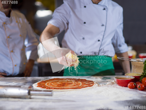 Image of chef sprinkling cheese over fresh pizza dough