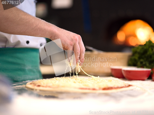 Image of chef sprinkling cheese over fresh pizza dough