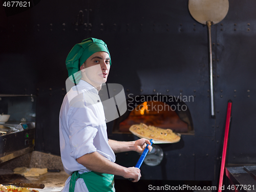 Image of chef putting delicious pizza to brick wood oven