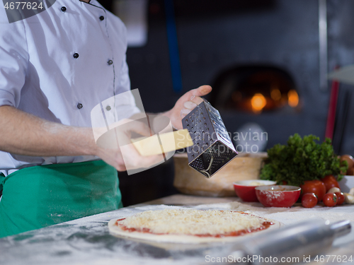 Image of chef sprinkling cheese over fresh pizza dough