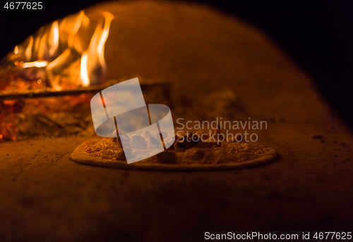 Image of chef putting delicious pizza to brick wood oven