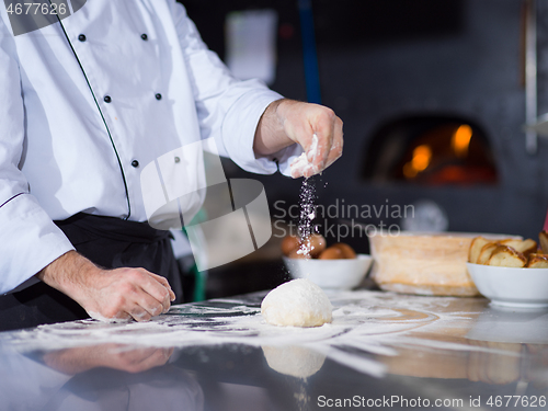 Image of chef sprinkling flour over fresh pizza dough