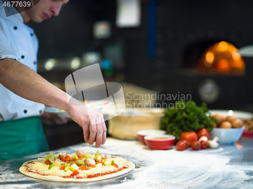 Image of chef putting fresh vegetables on pizza dough