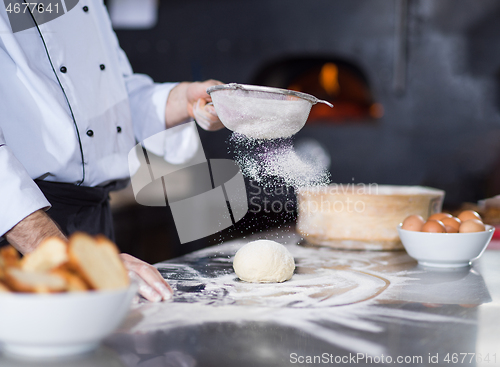 Image of chef sprinkling flour over fresh pizza dough