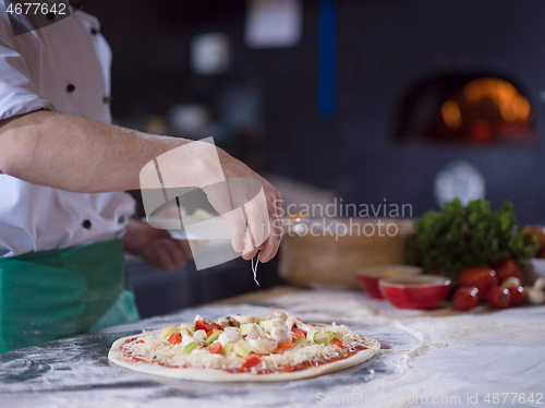 Image of chef putting fresh vegetables on pizza dough